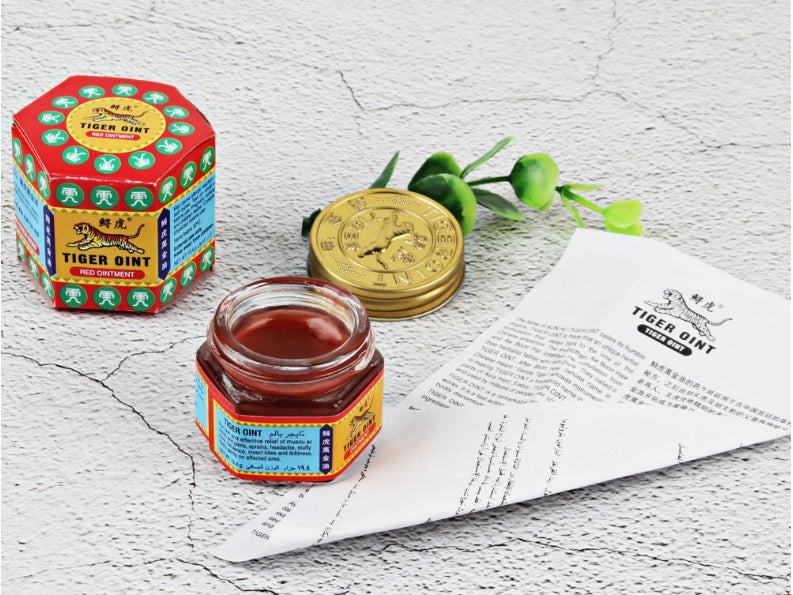 Tiger Balm jar and packaging on a textured surface with a leaf.