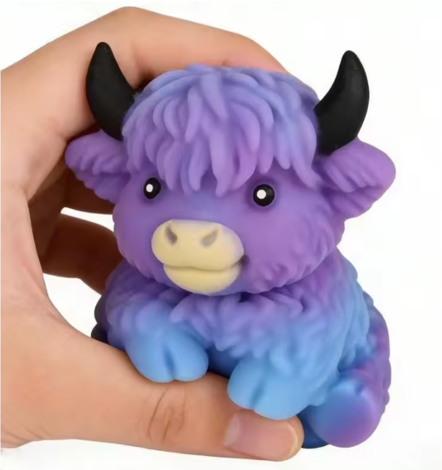 A small purple and blue fluffy cow figurine with black horns and a cream muzzle, being held in a person's hand against a white background.