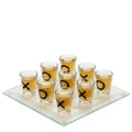 A drinking tic tac toe game with a glass board and multiple shot glasses arranged on top, with the shot glasses having 'X' and 'O' marks.